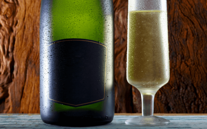 Bottom half of Champagne bottle beside a glass on a wooden background