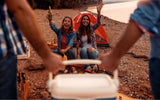 Two men holding a cooler to their campsite and two women greeting them
