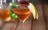 cocktail in a martini glass with apple garnish and apples in the background