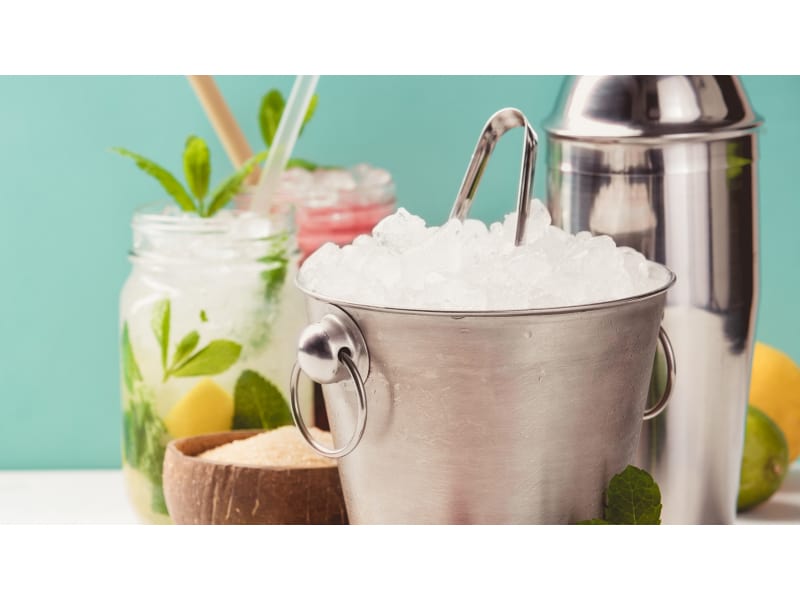 Ice bucket full of ice with tongs on top surrounded by a cocktail shaker and mason jars